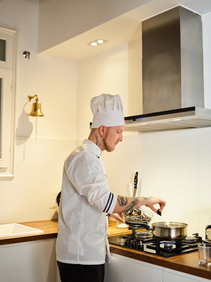 Side view of a male chef with tattoos cooking in a modern kitchen setting.